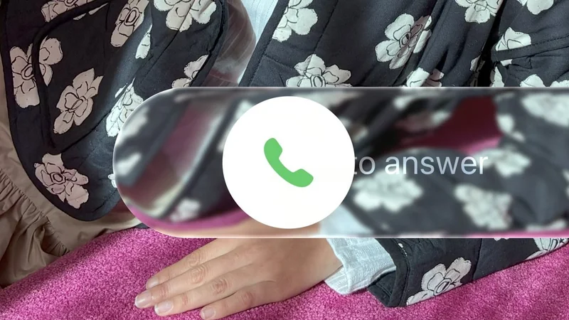 Hand resting on a pink blanket beside a person wearing a black floral-patterned robe, overlaid with a smartphone incoming call screen showing a green phone icon to answer