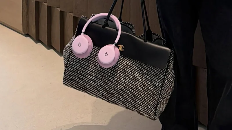 Person holding a black and white patterned handbag with black leather top, while pink Beats headphones hang from one handle, standing indoors on a smooth light-colored floor