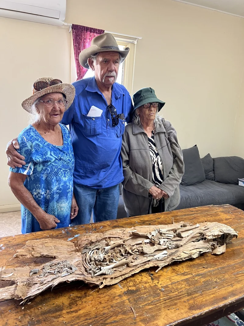 three elderly people stand behind a carefully arranged dingo skeleton lying on a table