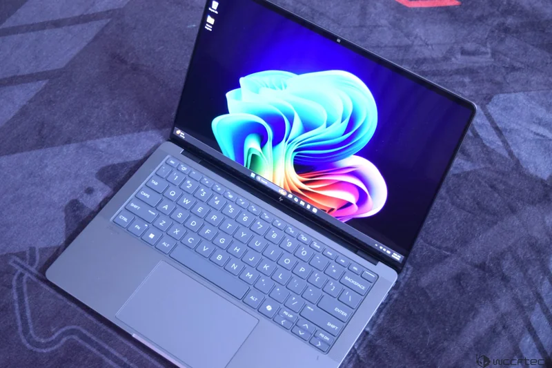 A HP laptop displaying the Windows 11 logo on its screen, resting on a textured surface with a visible 'wccftech' watermark