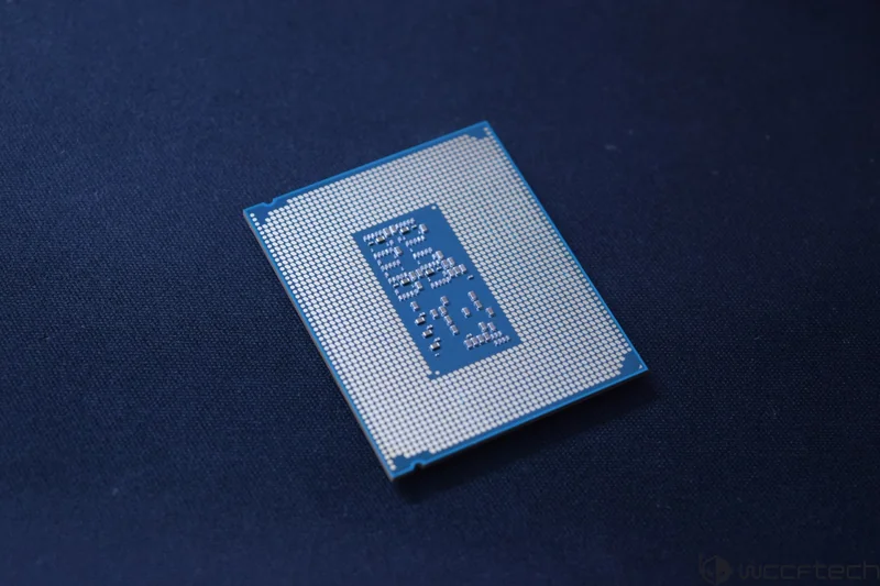 The close-up image shows the underside of an Intel CPU with visible pins and a blue substrate placed on a dark blue surface.