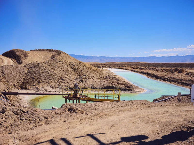 Image of a dry, plant less desert area. In amidst large lumps of soil sit a human-shaped pond of vivid blue water.