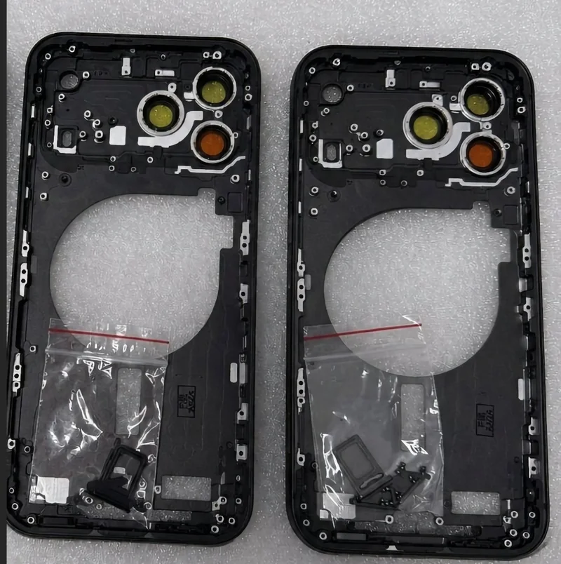 Two identical black smartphone back frames with three circular camera cutouts each, lying side by side on foam, with small clear plastic bags containing tiny components near the bottom.
