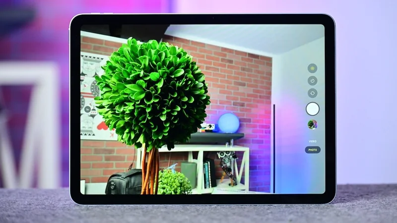 iPad Air M4 on a table displaying a large green topiary tree and a modern room with brick wall, shelves, and soft colorful lighting in the background.