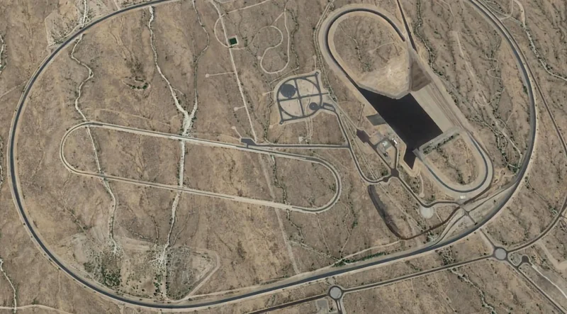Aerial view of a desert vehicle testing facility with large oval tracks, winding roads, and an elongated basin-like structure surrounded by barren rocky terrain