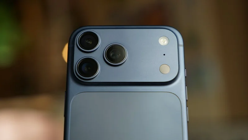 Close-up of a dark blue iPhone 17 Pro Max back showing three rear camera lenses, LED flash, and sensors on a raised rectangular camera module against a softly blurred background