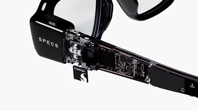 Close-up of high-tech black smart glasses arm, partially transparent to reveal internal electronic components and a small removable chip or module labeled with a stylized S logo