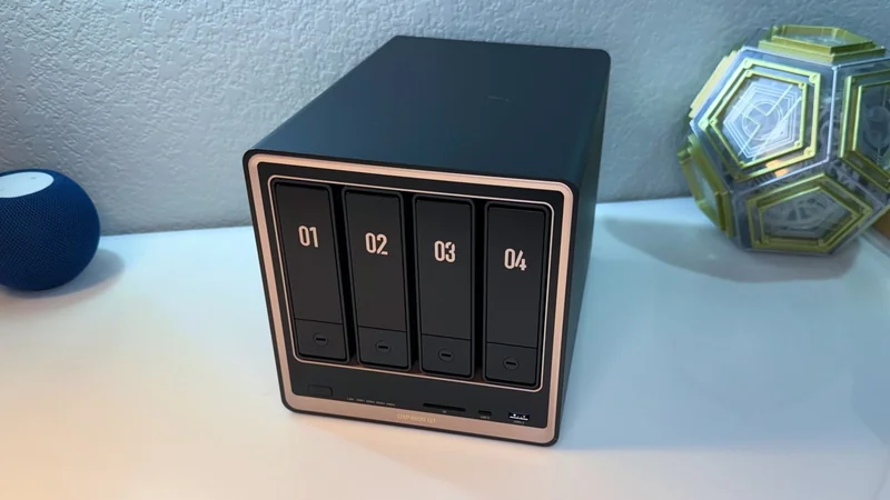 Black four-bay external storage enclosure labeled 01 to 04 on a white desk, with a decorative geometric light and a small blue sphere in the background