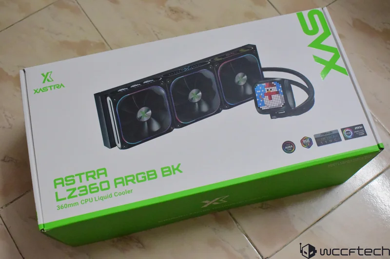 A Xastra Astra LZ360 ARGB BK 360mm CPU liquid cooler box on a tiled floor, showcasing the product image and logos for compatibility with Aura Sync, RGB Fusion, Polychrome Sync, and MSI Mystic Light.