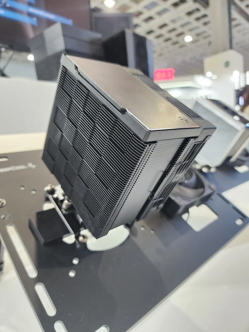 A large black CPU cooler with stacked fins is displayed on a mounting bracket at an exhibition booth.