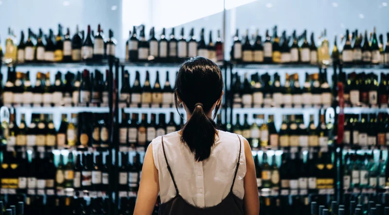Image of a woman looking at a large store rack filled with wine bottles.