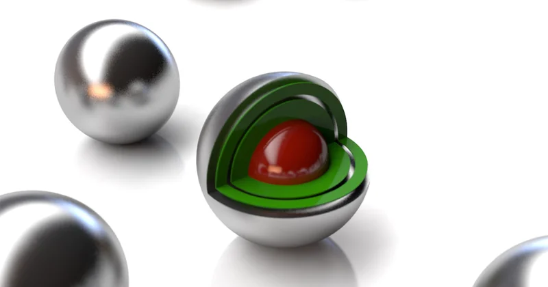 Image of a set of silvery balls, one of which has a cutaway showing layers of green and a red core.