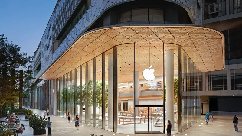 Modern Apple Store with tall glass walls, glowing Apple logo, two-story interior, wooden ceiling, trees inside and outside, and people walking across a spacious urban plaza