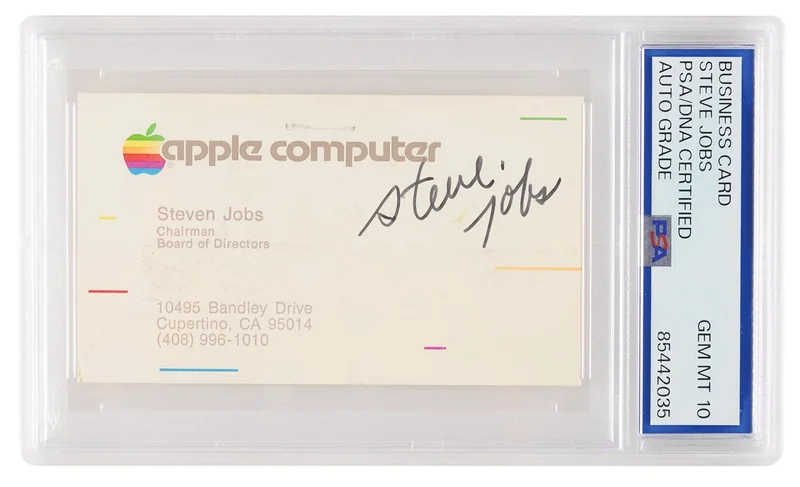 Encased Apple Computer business card featuring multicolor apple logo, Steven Jobs contact details, and prominent black autograph, graded and sealed in a clear plastic holder with certification label