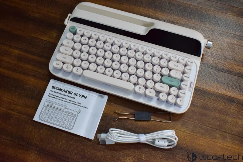 The Epomaker Glyph keyboard is shown with a user manual, keycap puller, and USB cable on a wooden surface.