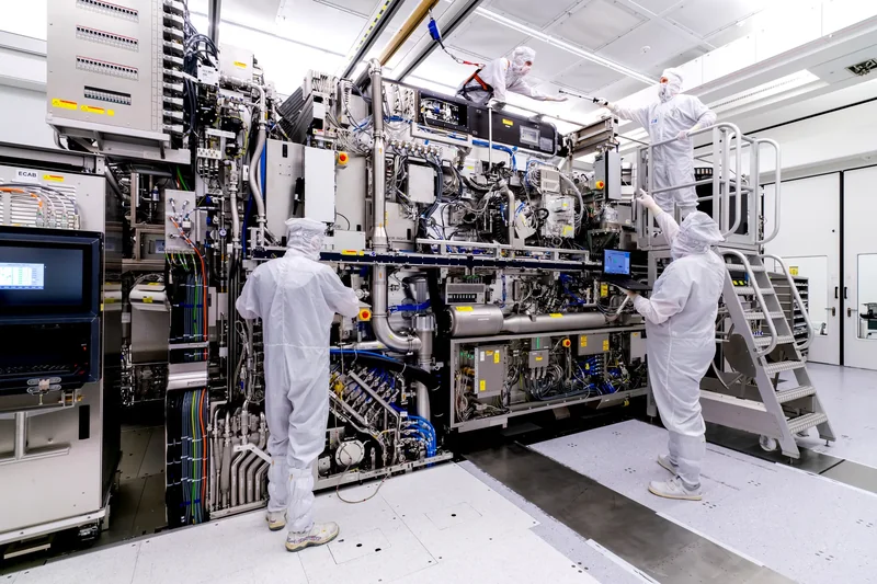 Technicians in cleanroom suits working on a large semiconductor manufacturing machine.