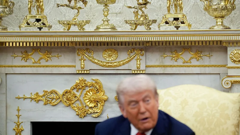 President trump seated before a wall covered in gold leaf and decorations.