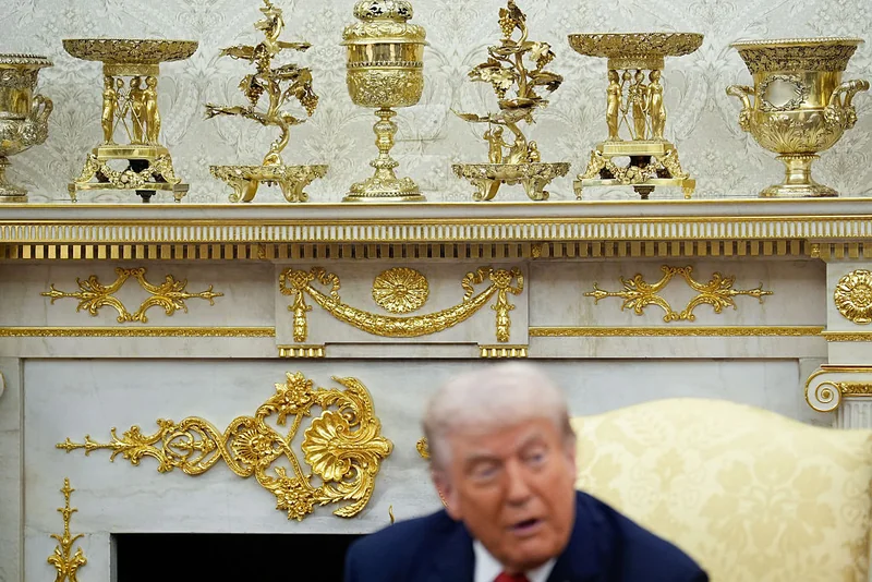 President trump seated before a wall covered in gold leaf and decorations.