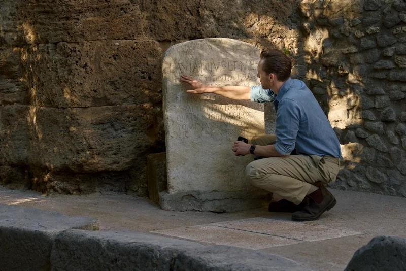 Tom Hiddleston examines an inscription at the Gatehouse ruins in Pompeii.