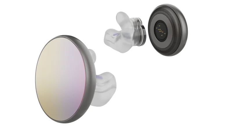 Exploded view of a sleek round wireless earbud, showing reflective outer face, inner electronics, and clear silicone ear tip separated in alignment on a plain white background