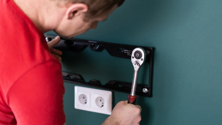 Person using a ratchet to secure a TV wall-mount bracket to a wall.