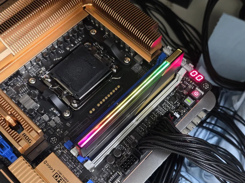An ASUS ROG motherboard featuring a Lotes socket, RGB RAM, copper heatsinks, and a digital readout displaying '00'.