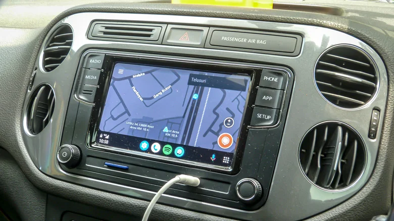 A car head unit showing an Android Auto connection, with maps, and a USB cable attached.