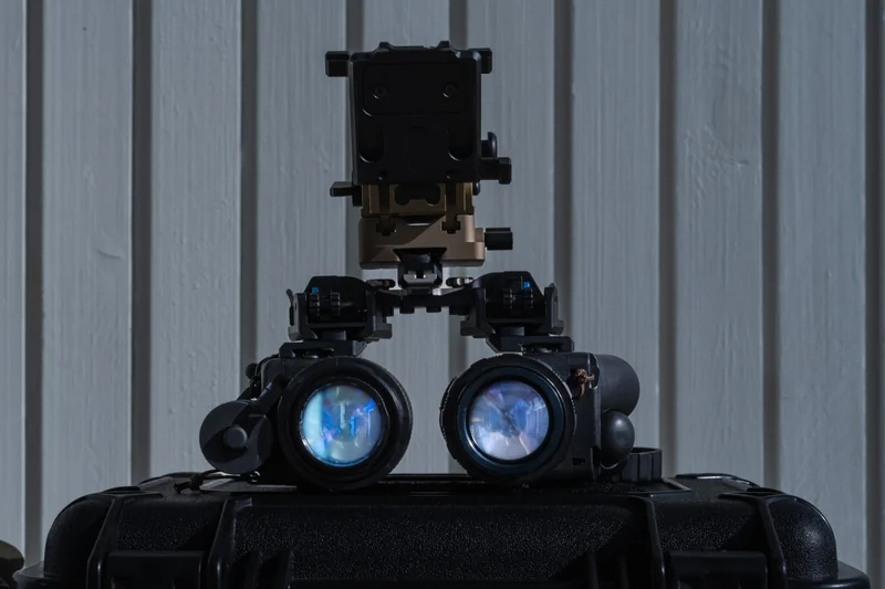 Front view of modern binocular night vision goggles (NVG) with a mount, sitting on top of a black protective case.