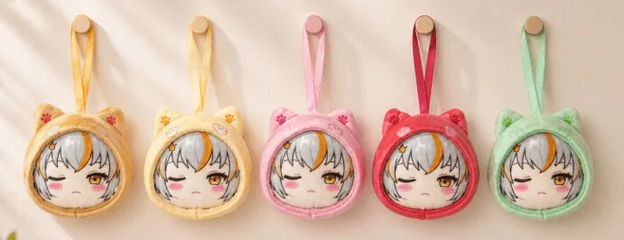 Five plush keychains with winking cartoon faces and animal ear hoods in yellow, orange, pink, red, and green hang in a row.