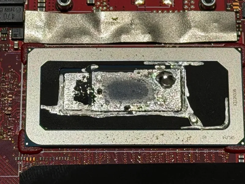A close-up image of an unbranded, delidded processor module on a red circuit board, showing exposed internal components with residue from thermal paste.