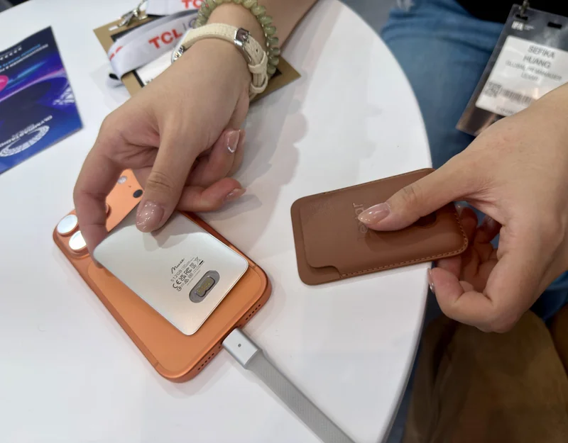 A person inserts a Lexar memory card into a brown Lexar card holder, with a TCL lanyard and smartphone visible on the table.