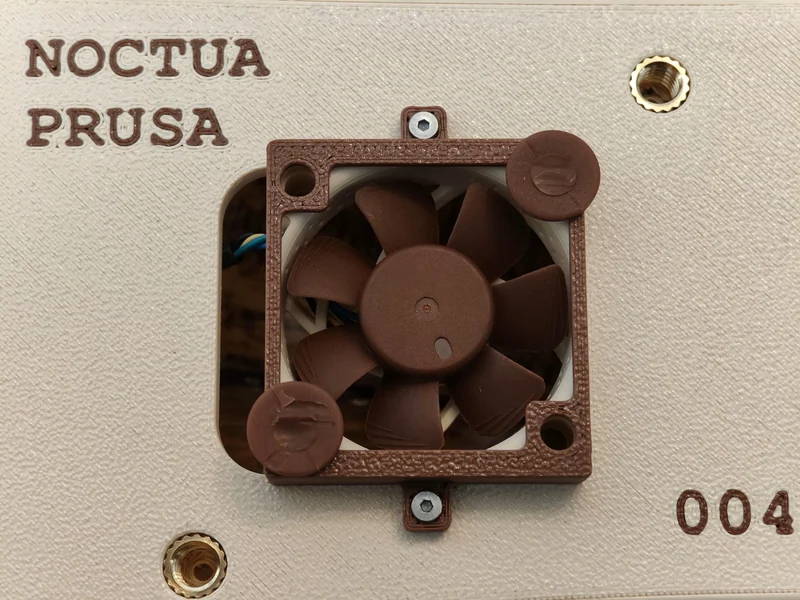 A Noctua cooling fan is mounted on a beige Prusa 3D printer panel, with the text 'NOCTUA PRUSA' and a serial number '004'.