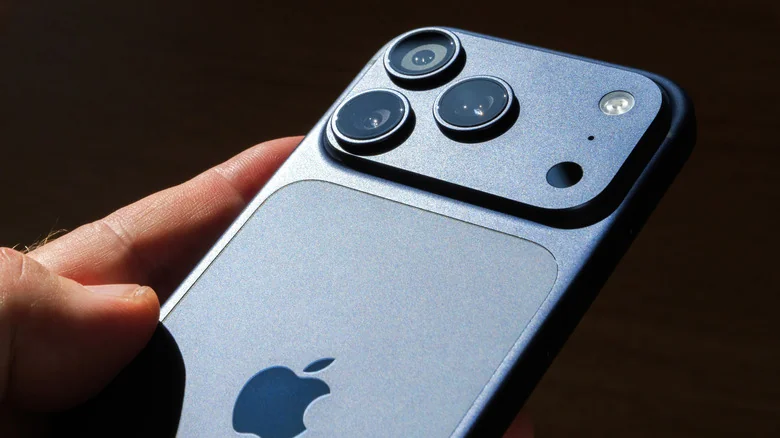 A hand holds up the back of a sleek iPhone against a dark background.