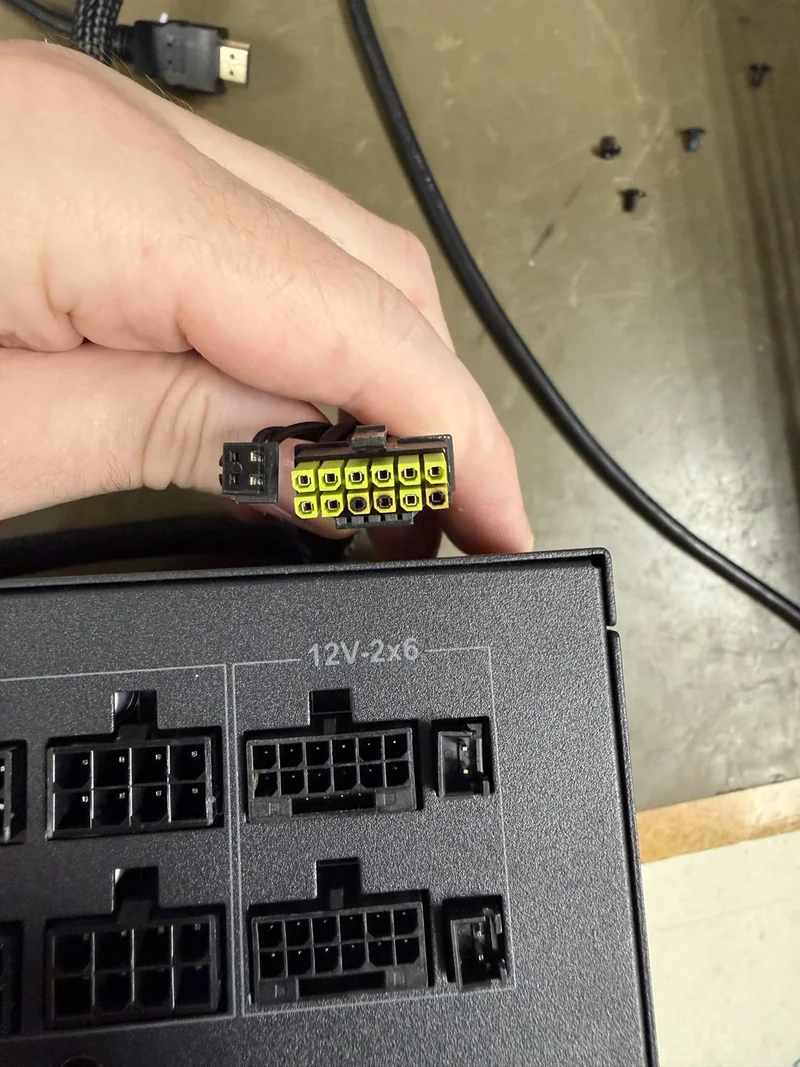 A hand holding a 12V 2x6 power connector above a power supply unit labeled '12V-2x6.'