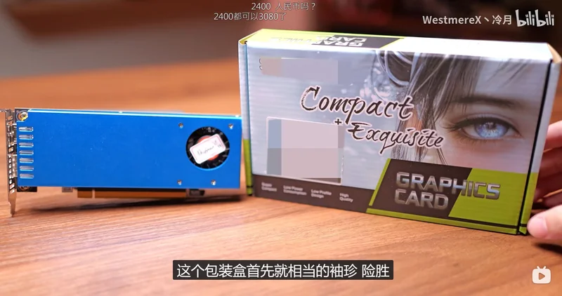 An unbranded blue graphics card sits next to its box labeled 'Compact + Exquisite GRAPHICS CARD' on a wooden surface.