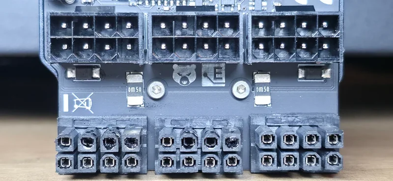 A close-up view of a graphics card power connector area showing four 8-pin power sockets, with visible markings including a bear logo and the letters 'E' and '0m50'.