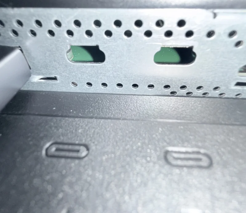 A close-up of a metal panel with ventilation holes and visible USB-C port markings on a piece of hardware.