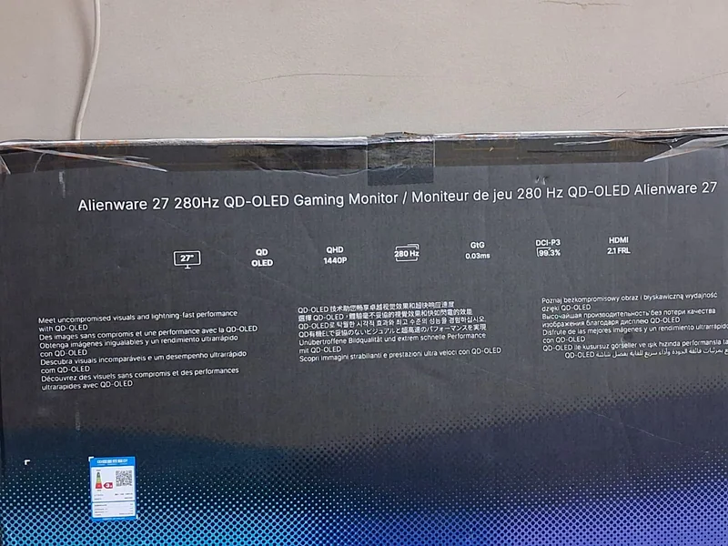 The image shows packaging for an Alienware 27 280Hz QD-OLED gaming monitor featuring specifications like a 27-inch display, QHD 1440p resolution, 0.03ms response time, DCI-P3 99.3% color accuracy, and HDMI 2.1 compatibility.