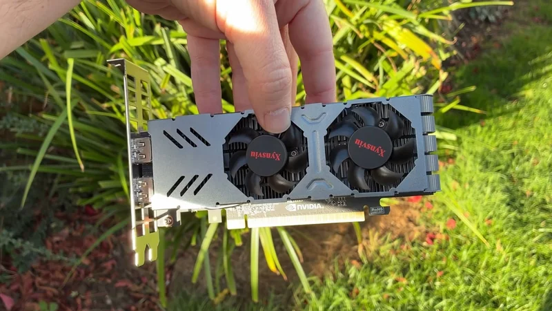A person holds a Masuax graphics card with dual fans and visible NVIDIA branding outdoors.