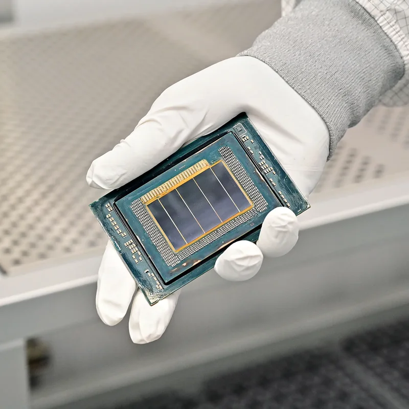 A gloved hand holding an unbranded processor chip displaying multiple silicon dies.