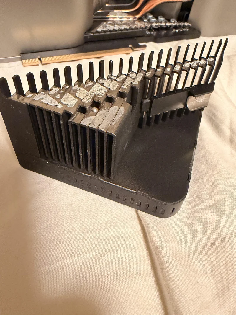 A detailed close-up of a large, unbranded heat sink with cooling fins, placed on a beige surface, with thermal paste residue visible on the contact area.