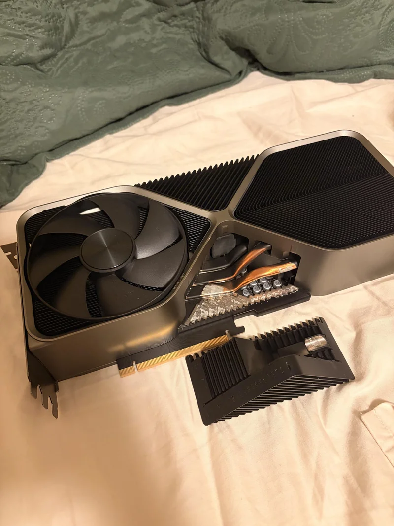 A disassembled NVIDIA graphics card with a large cooling fan and visible heat pipes on a bed.