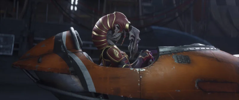An alien character sits in an orange and silver space vehicle cockpit in a sci-fi setting.