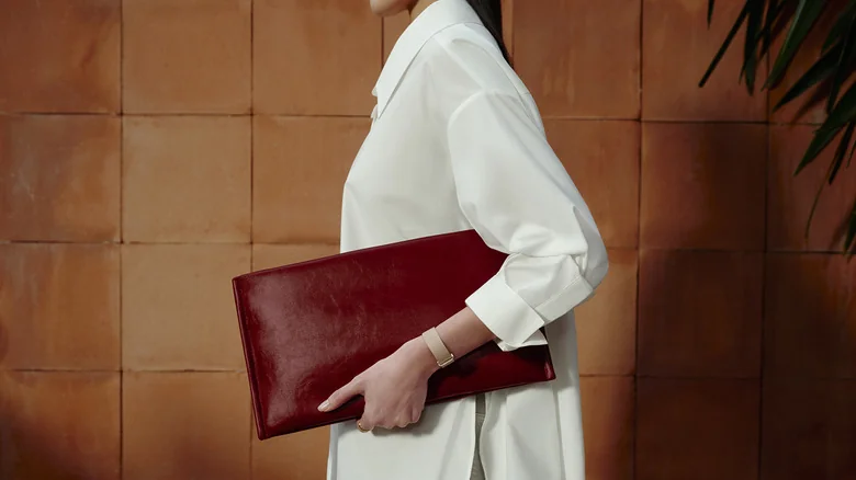 The side profile of a woman wearing a beige Fitbit Air and holding a maroon bag.